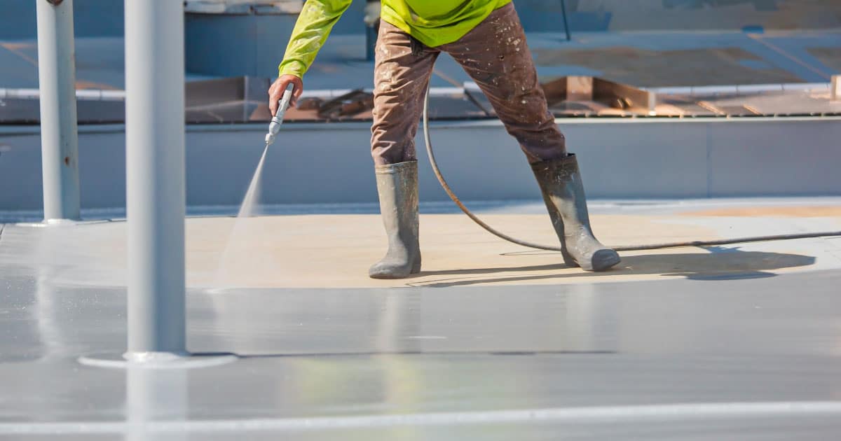 Roofer applying spraying white coating onto flat roof