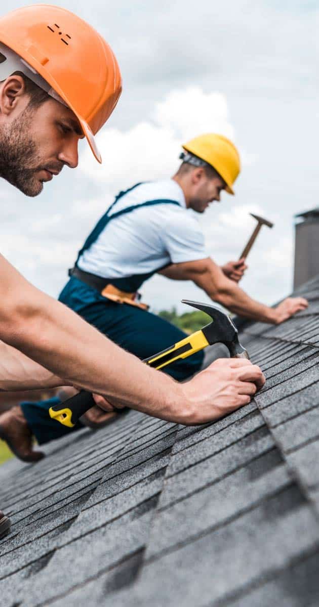 Two roofers installing new asphalt tile roofing
