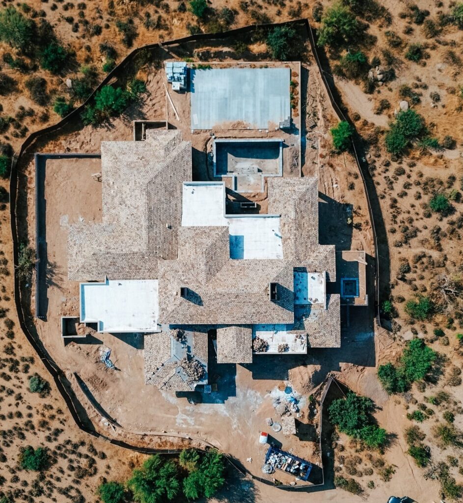 Aerial view of a luxury home under construction in the Arizona desert, showcasing high-end roofing installation and premium architectural design.
