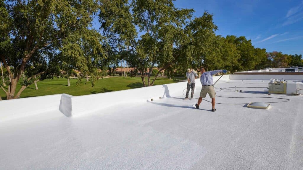 Two roofers inspecting white foam roof on Phoenix commercial building to assess repair costs