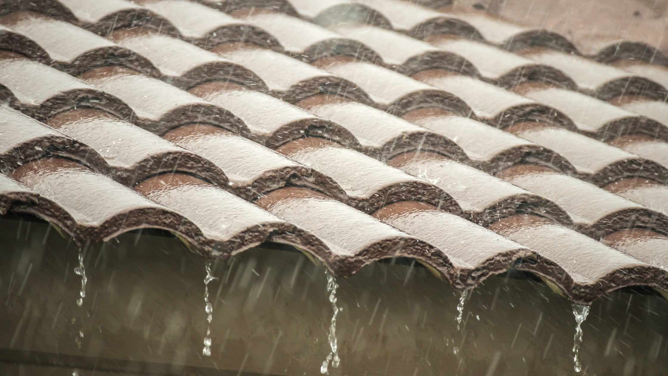 Water dripping from damaged tile roof during Arizona monsoon rain showing need for repair